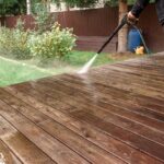 Man cleaning walls and floor with high pressure power washer. Washing terrace wood planks and cladding walls.
