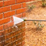 Dirty brick wall being cleaned with a pressure washer.